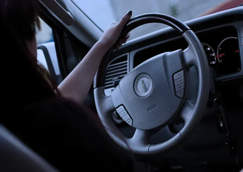 Driver’s hands on a steering wheel inside a car, dashboard visible in dim light