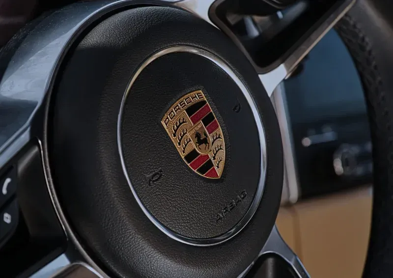 Close-up of a Porsche steering wheel with the gold, black, and red crest on the center hub