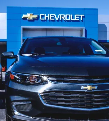 Black Chevrolet sedan parked in front of a Chevrolet dealership sign