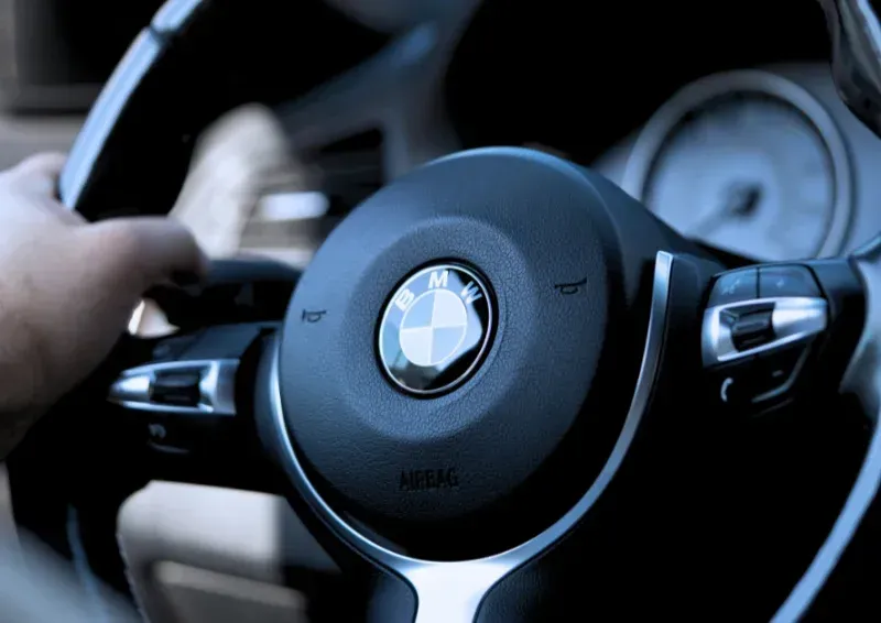 Close-up of a BMW steering wheel with a hand on the wheel inside a car interior.