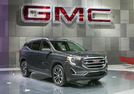 Silver GMC SUV on display in a showroom beneath a large GMC logo.