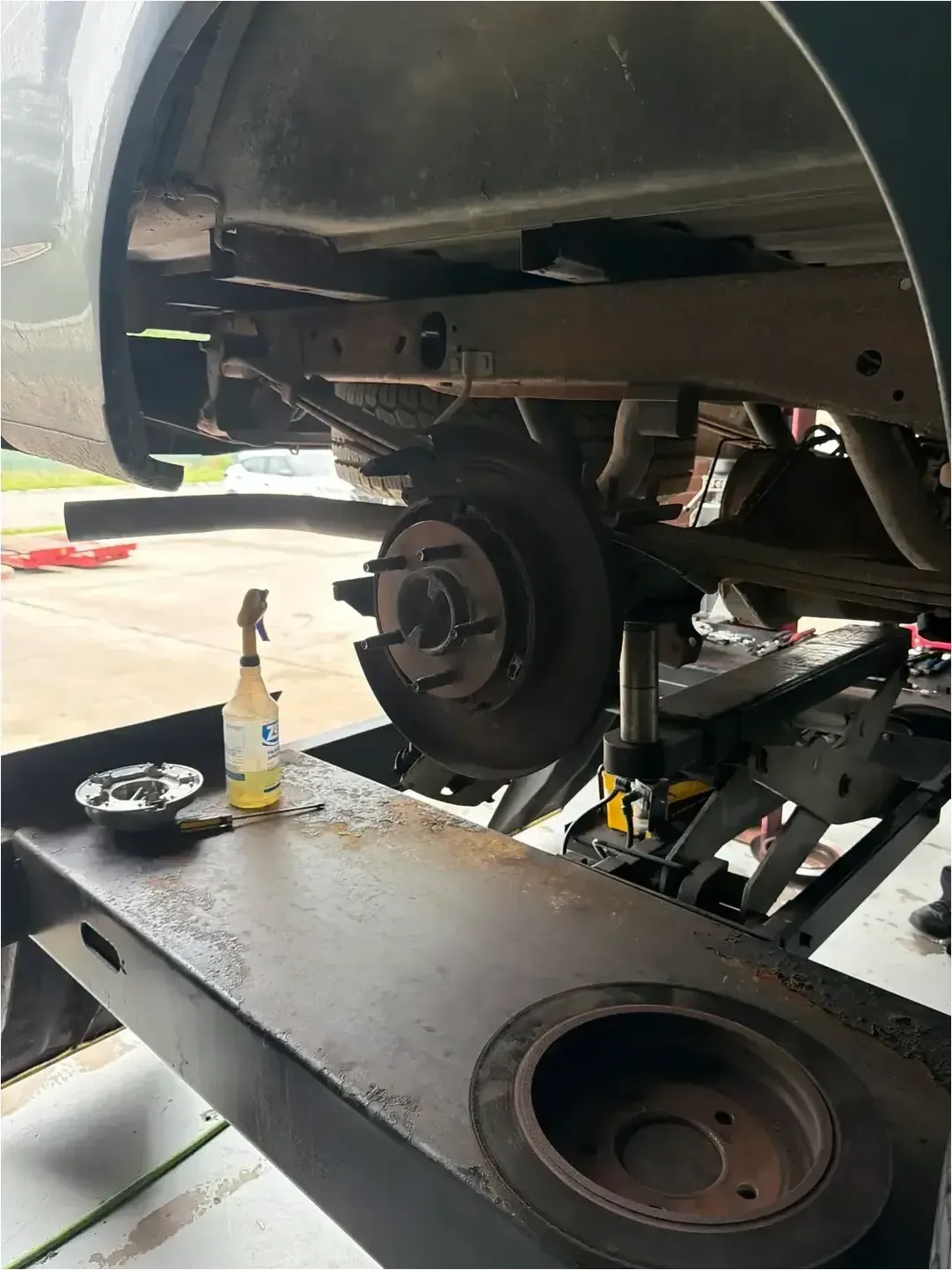 Mechanic removing a brake drum from a vehicle wheel, with hands over a bucket in a garage.