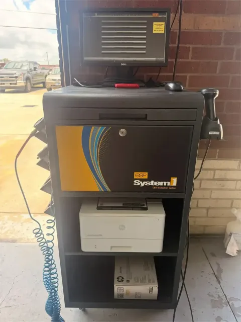 Black kiosk cabinet with a touchscreen, printer, and keypad in a garage-like space