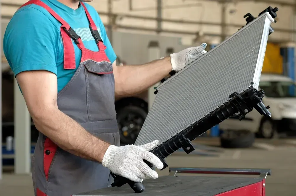 Worker in gloves holding a car radiator in a workshop