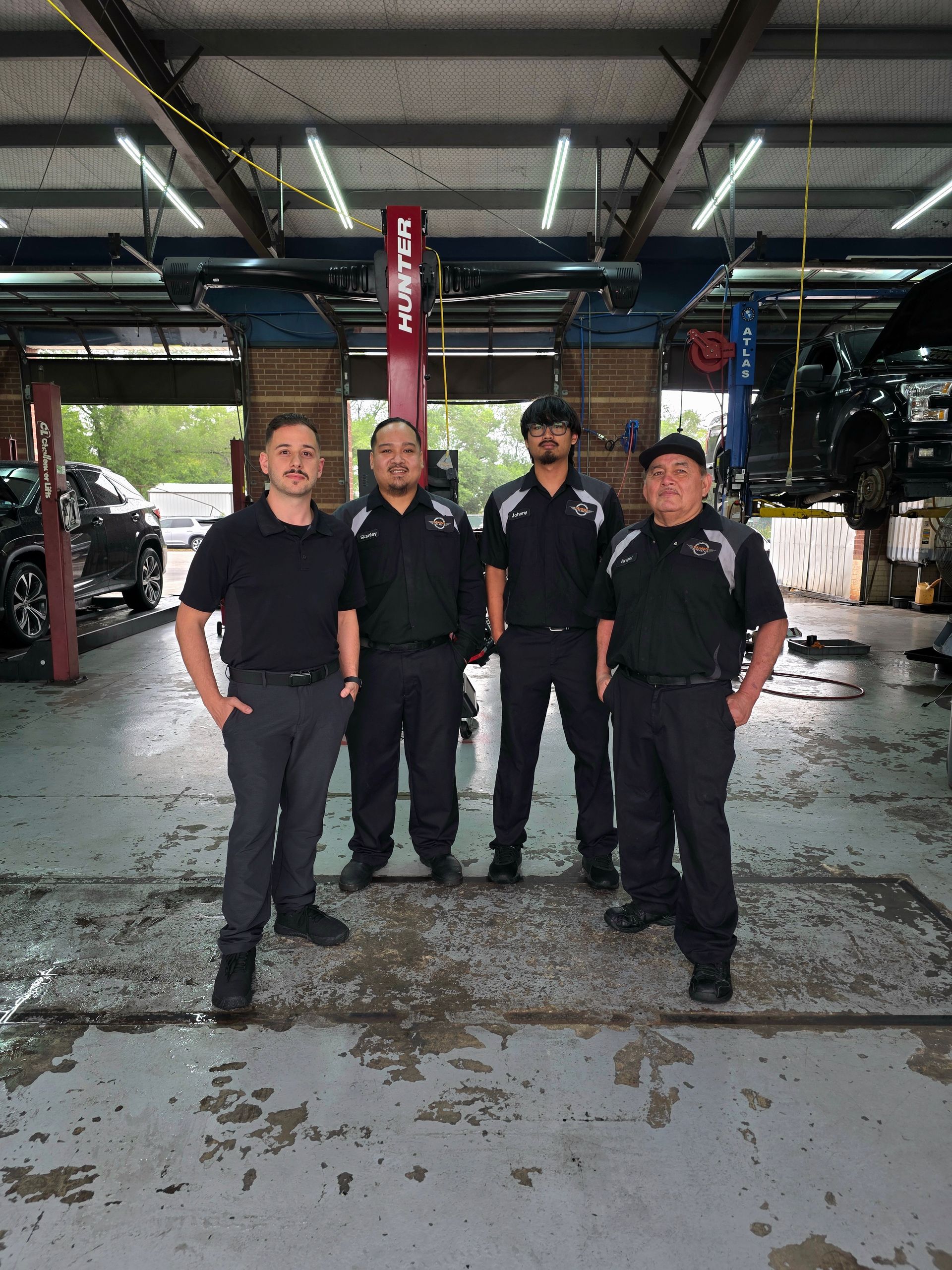Four people in black uniforms standing together in a covered parking area with blue flooring.