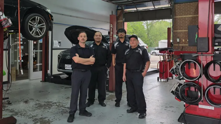 Three mechanics standing in an auto repair shop in alvin texas under lifts, with a car raised in the background.