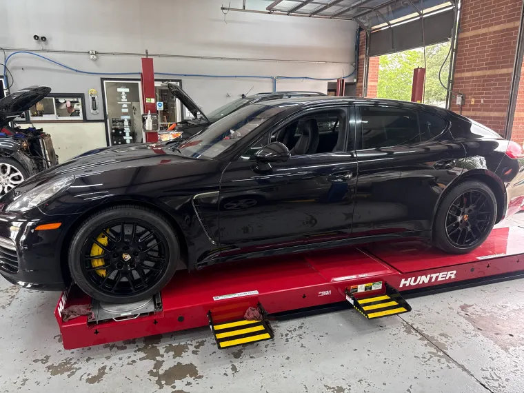 Black sports sedan on a red car lift in a garage, with yellow wheel chocks underneath.