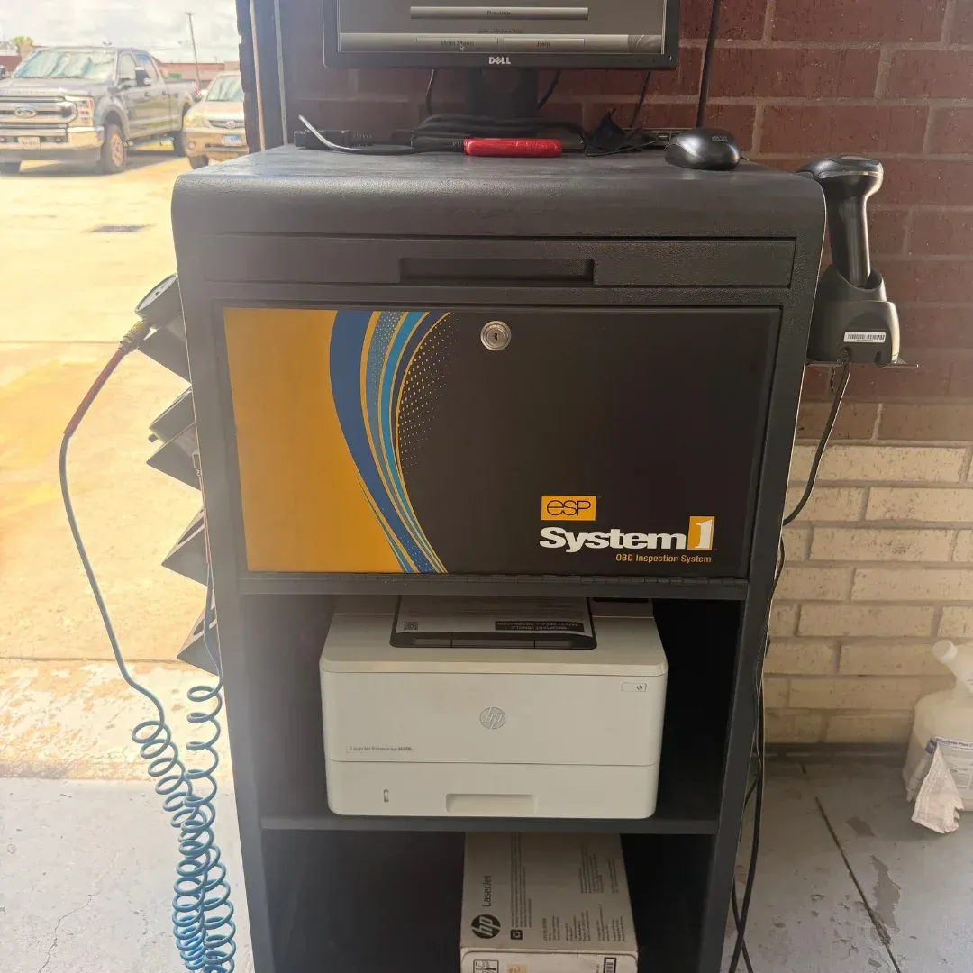 Black kiosk stand with small printer and monitor in a brick-walled indoor space