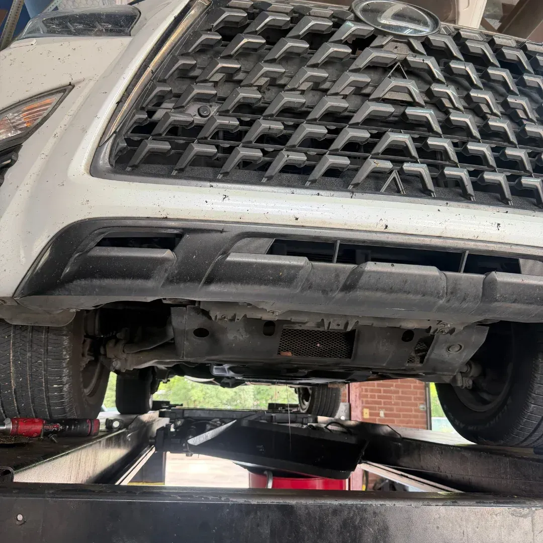 Mechanic working under a black SUV on a lift in an auto repair shop