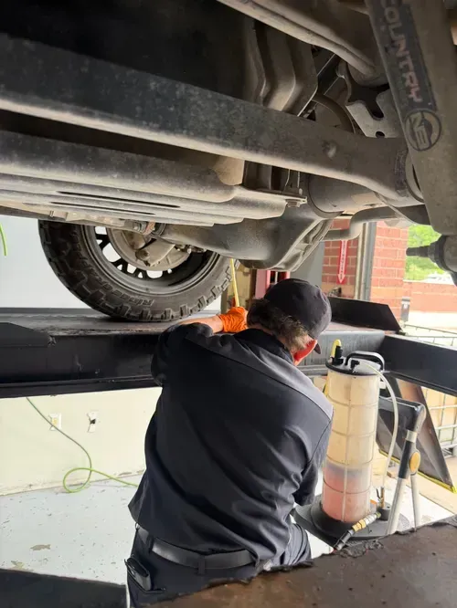 Mechanic working under a raised car in a garage, with tools and equipment nearby