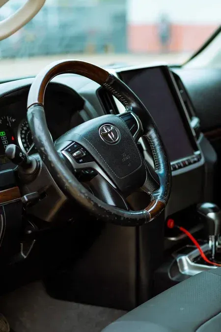 Car interior with steering wheel, dashboard screen, and center console with a red cable and cup holder.