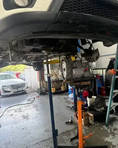 Car lifted in auto shop, mechanics working underneath with tools and equipment nearby