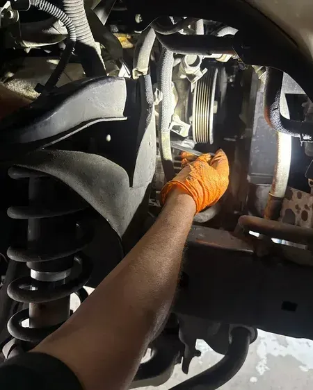 Mechanic’s gloved hand adjusting a car’s belt and pulley under the hood