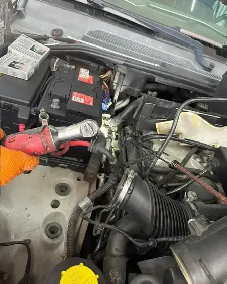 Car battery bay with a red flashlight and exposed wiring under the hood