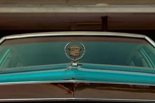 Close-up of a turquoise classic car hood with a Cadillac emblem on the front grille.