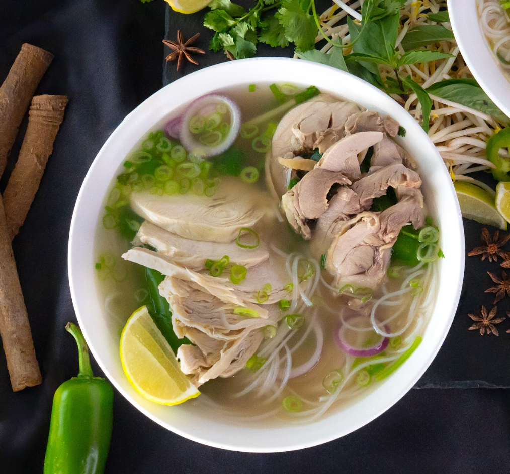 Bowl of noodle soup with sliced meat, lime wedge, and scallions on a dark table