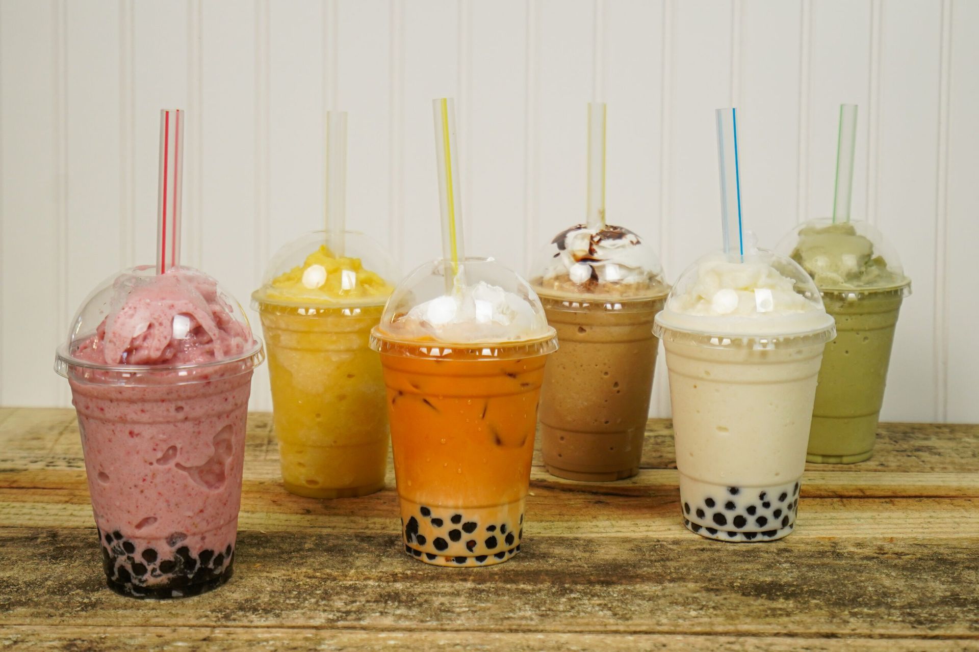 Six colorful bubble tea drinks with boba lined up on a wooden table