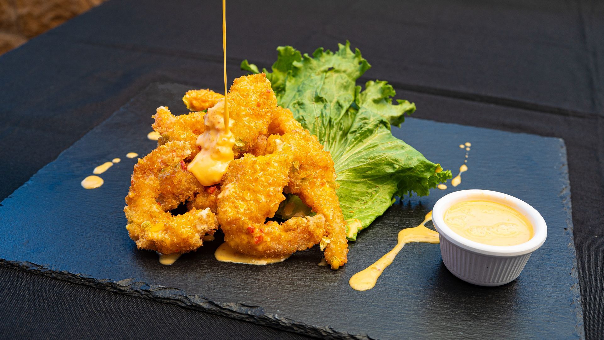 Fried bite-sized appetizer on a slate plate with greens and a small cup of dipping sauce