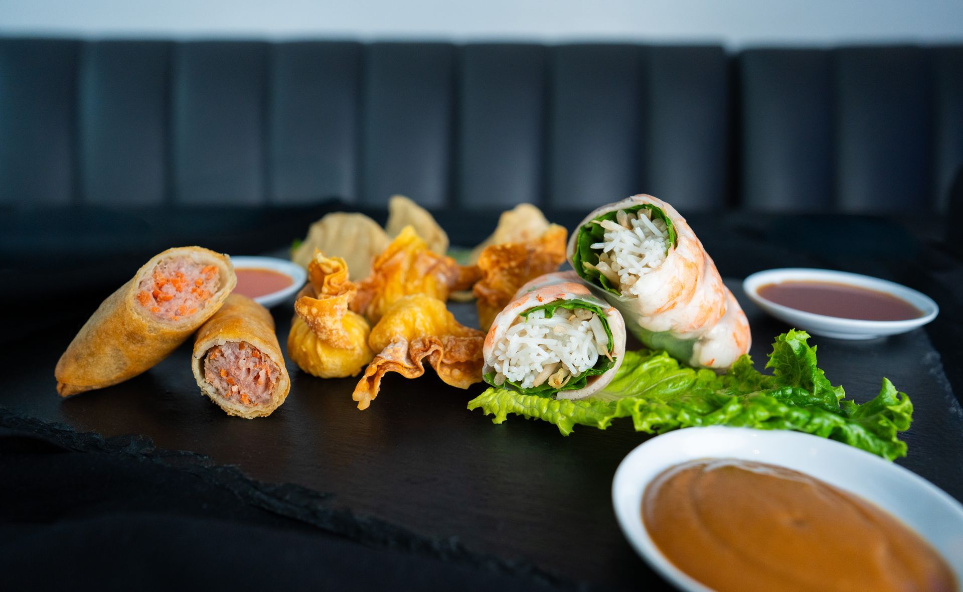 Assorted fried appetizers and spring rolls on a dark table with dipping sauces