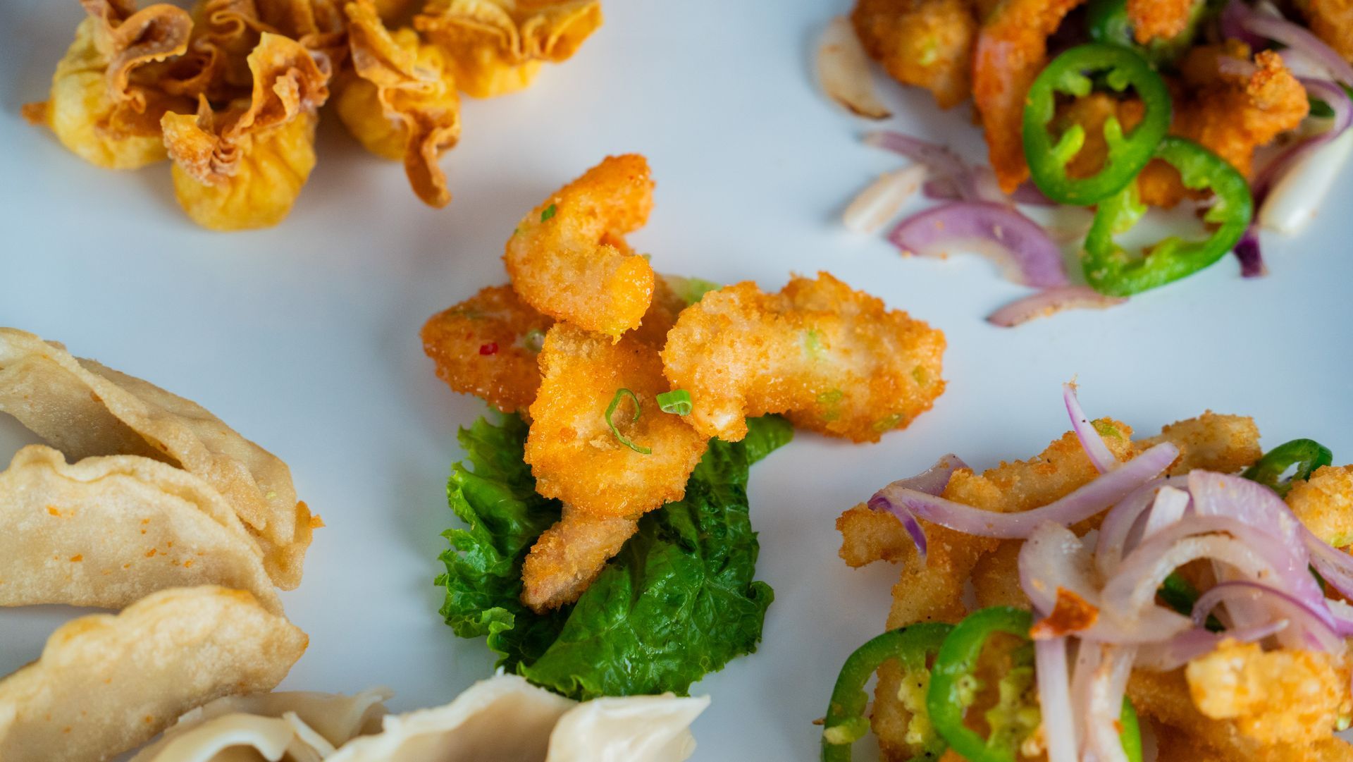 Assorted fried appetizers on a light table, including broccoli, shrimp, dumplings, and sliced peppers with onions