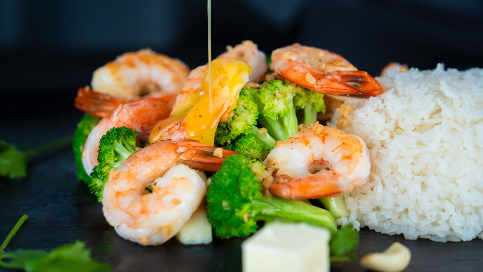 Shrimp, broccoli, and white rice on a black plate, with a side of sauce and lime