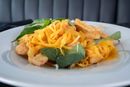 Pasta with golden sauce, chicken pieces, and fresh basil on a white plate