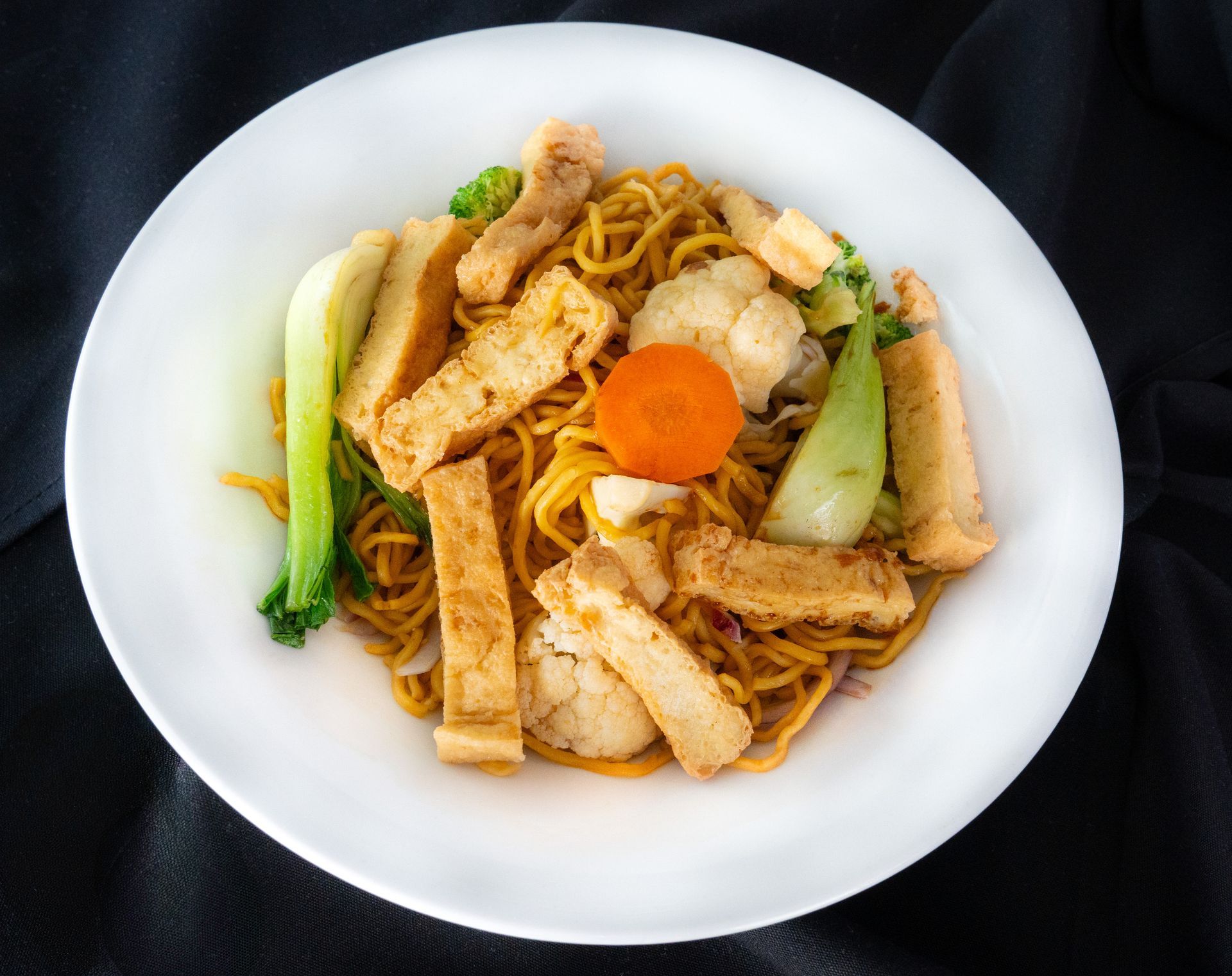 Plate of stir-fried noodles with tofu, carrots, and bok choy on a white dish