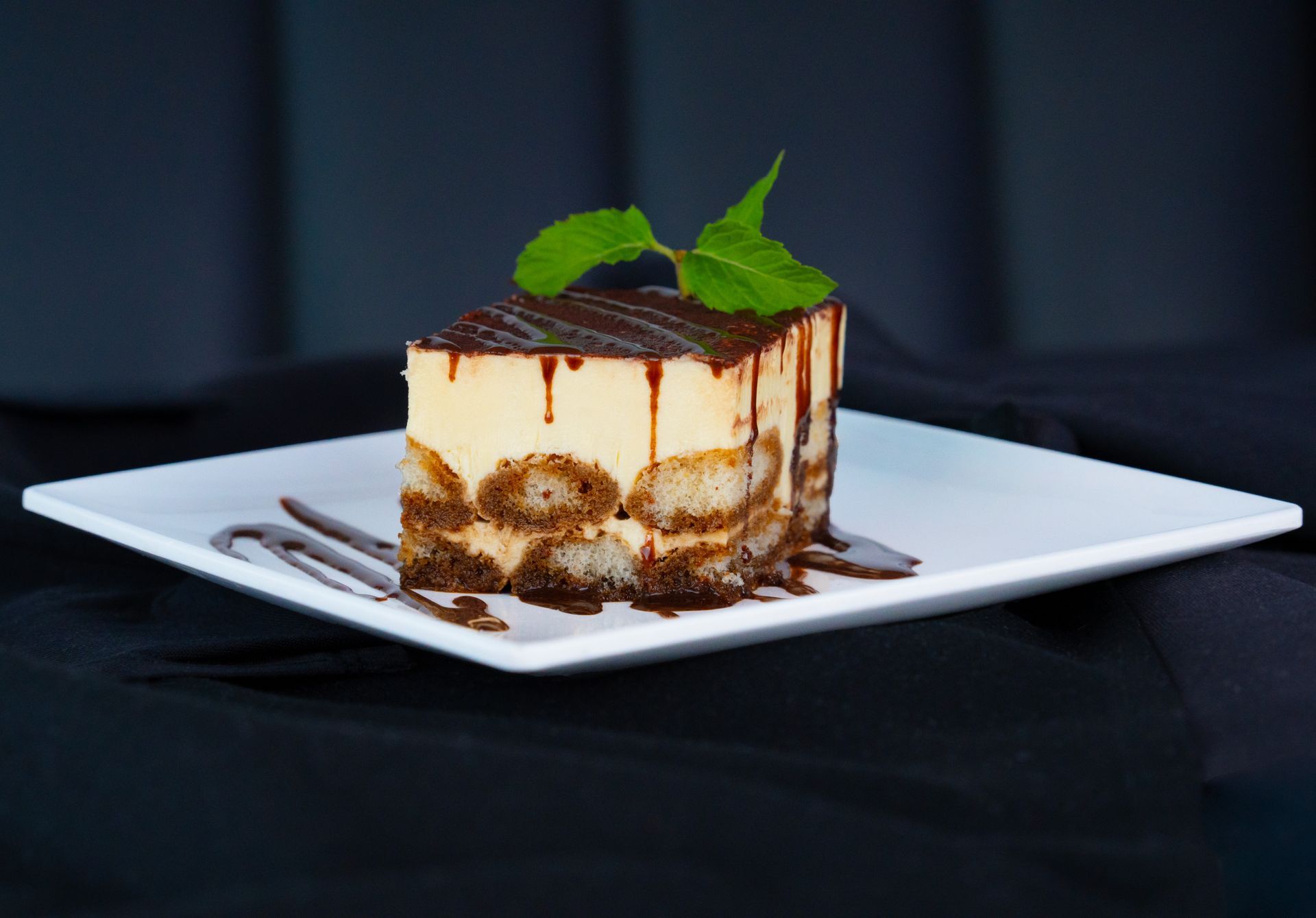 Chocolate-topped tiramisu on a white plate, garnished with mint leaves
