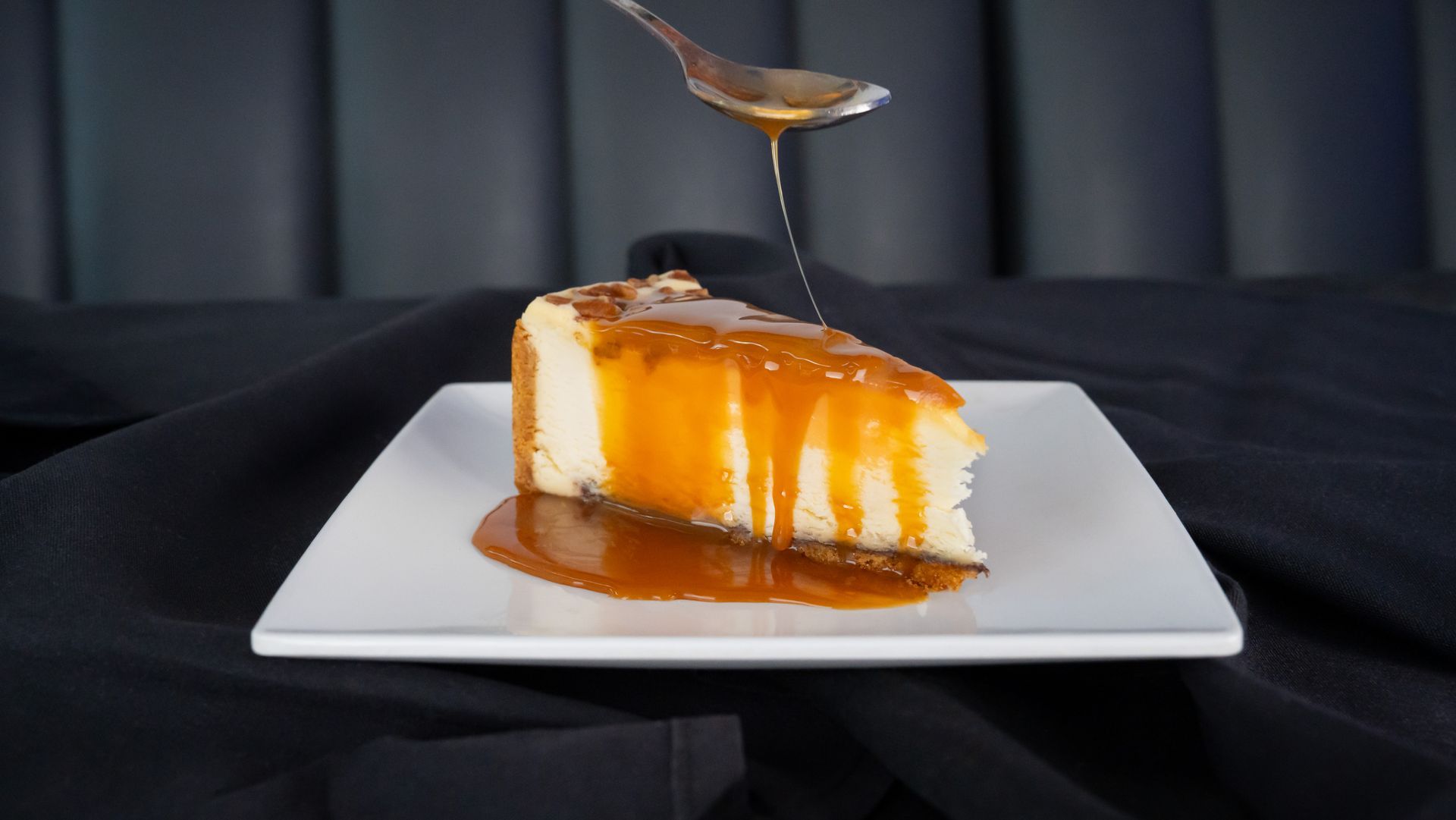 Slice of caramel-drizzled cheesecake on a white plate with a fork above it