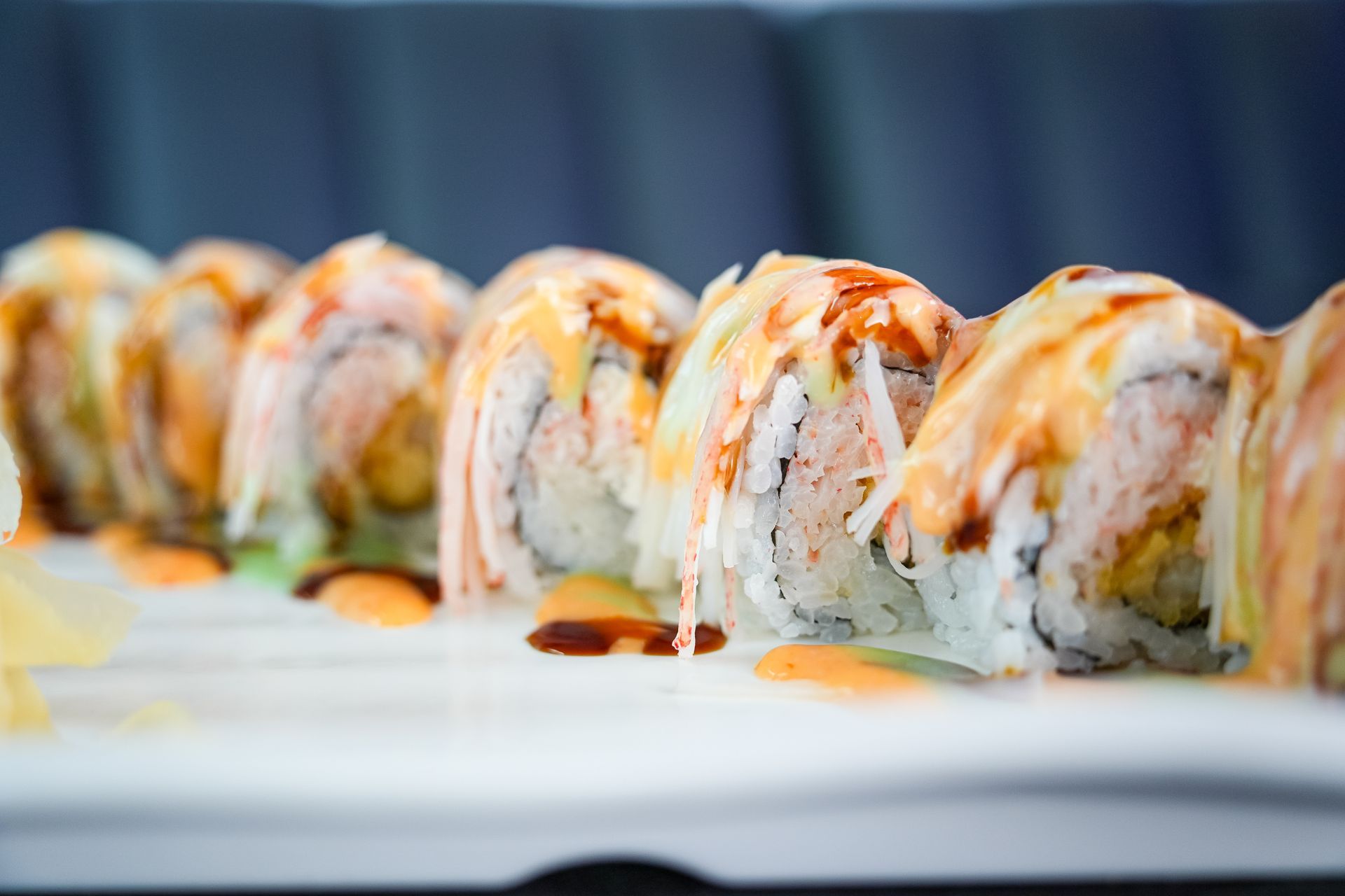 Sushi rolls topped with sauce on a white plate, arranged in a row