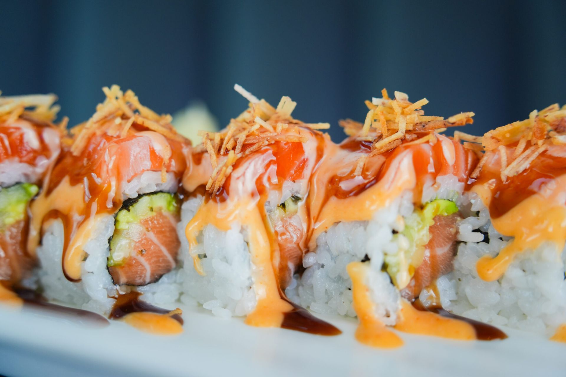Sushi rolls topped with orange sauce and white drizzle on a white plate