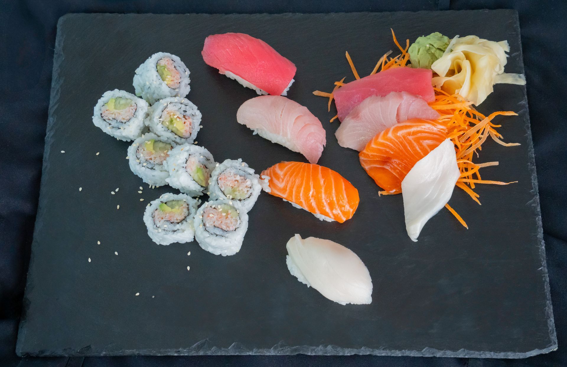 Assorted sushi rolls and nigiri arranged on a black slate platter with orange garnish