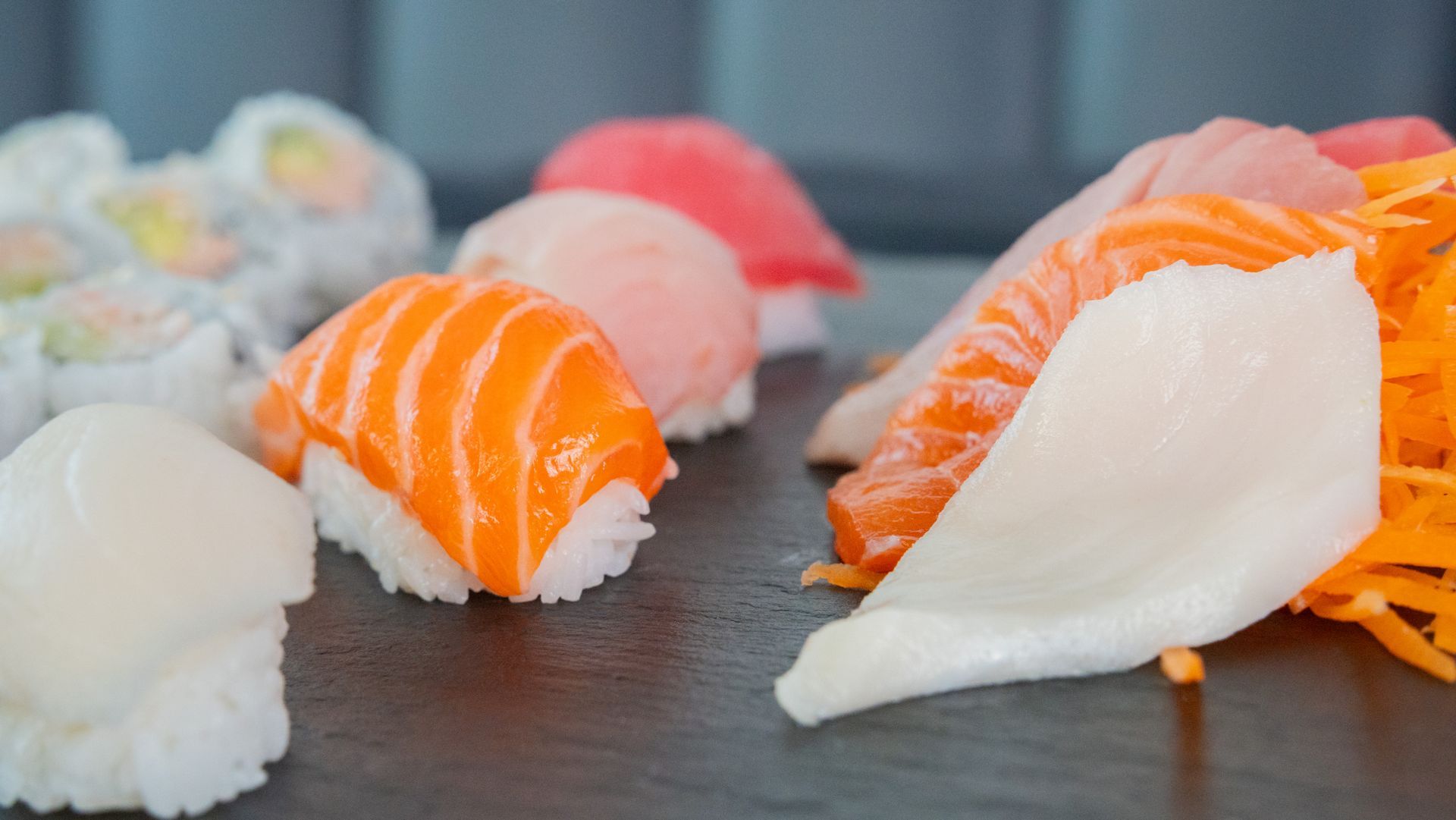 Assorted sushi nigiri on a dark plate, including salmon and white fish with orange garnish