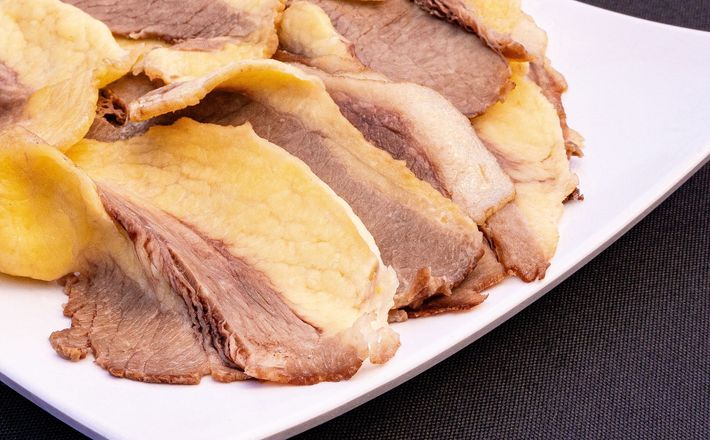 Thin slices of raw red meat on a white plate, arranged in overlapping layers