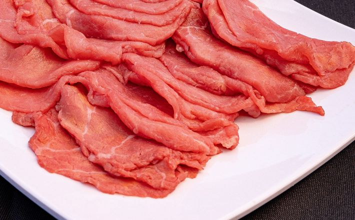 Thin slices of raw red meat on a white plate, arranged in overlapping layers