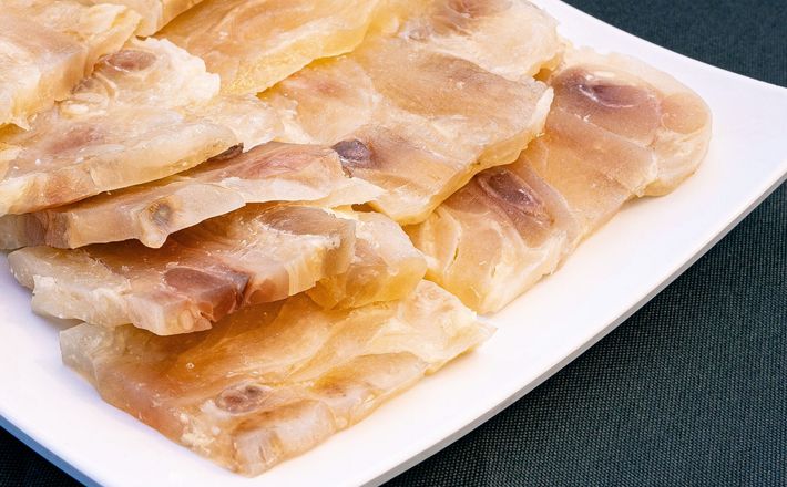Thin slices of raw red meat on a white plate, arranged in overlapping layers