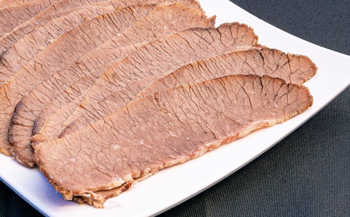 Thin slices of raw red meat on a white plate, arranged in overlapping layers