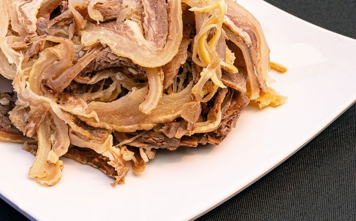Thin slices of raw red meat on a white plate, arranged in overlapping layers
