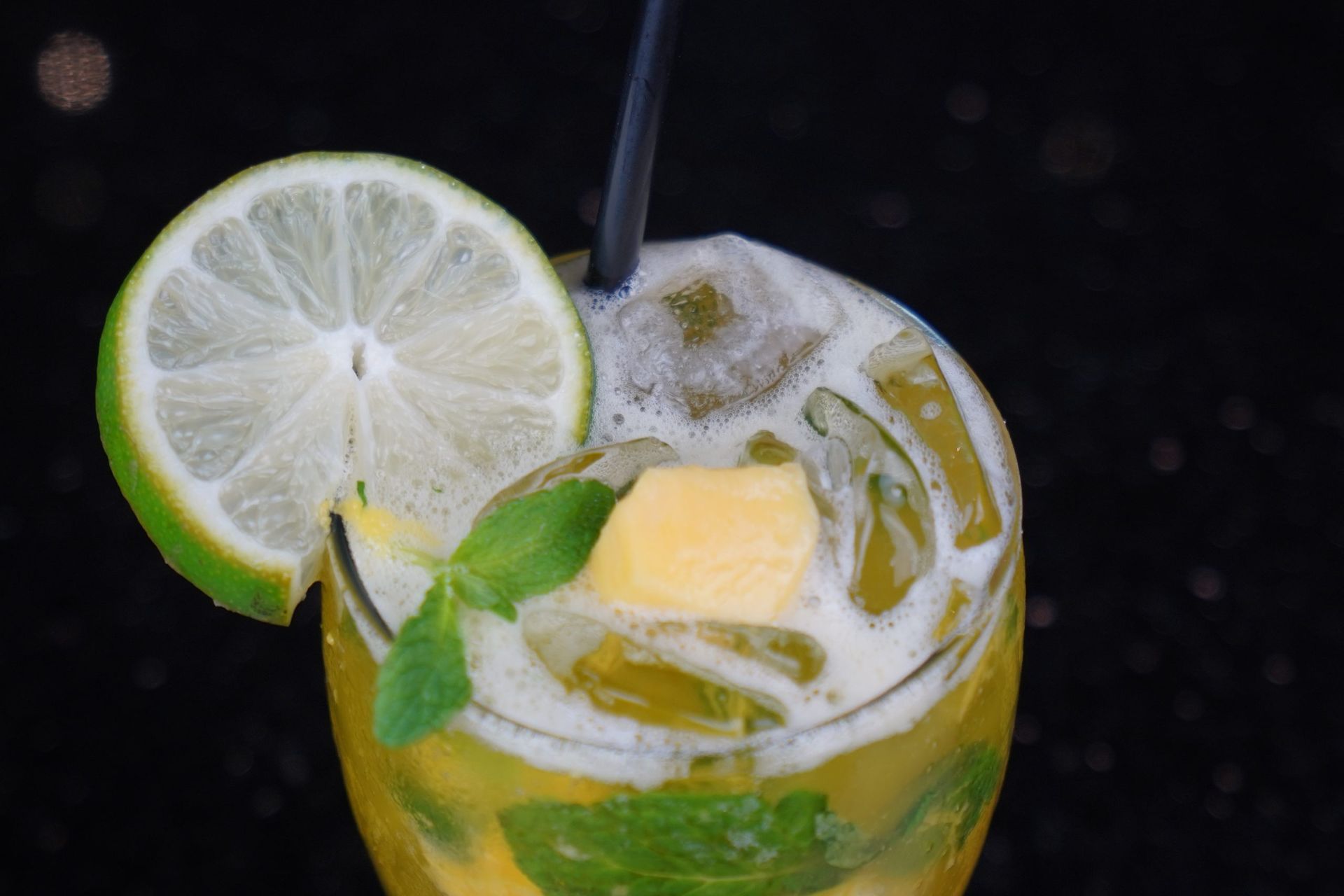 Mojito in a glass with lime slice, mint, ice, and black straw against a dark background