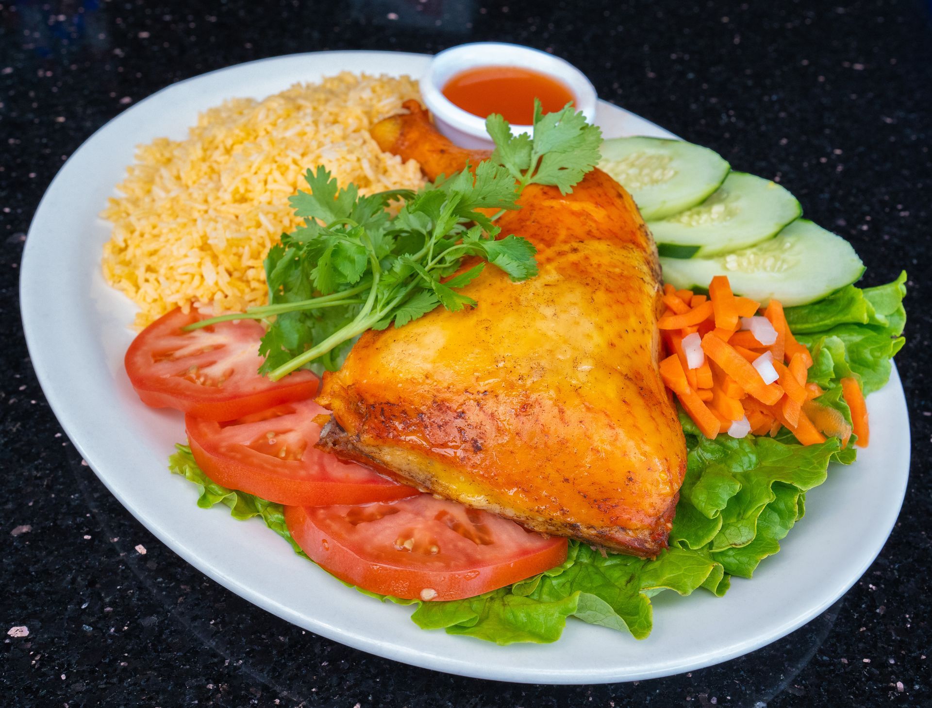 Grilled chicken with rice, tomato, cucumber, lettuce, and dipping sauce on a white plate
