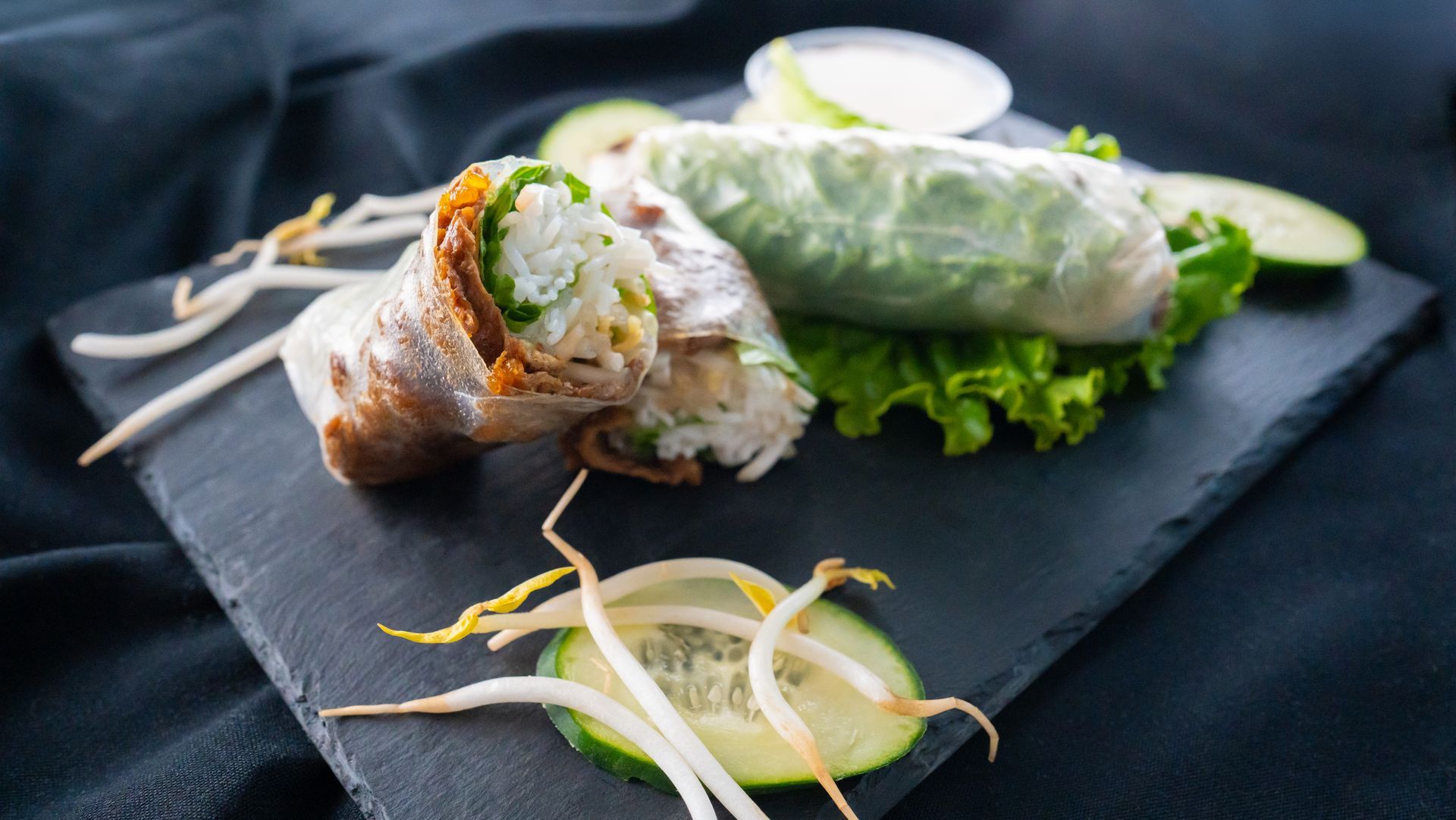 Vietnamese spring rolls on a black slate plate with lettuce, herbs, and dipping sauce