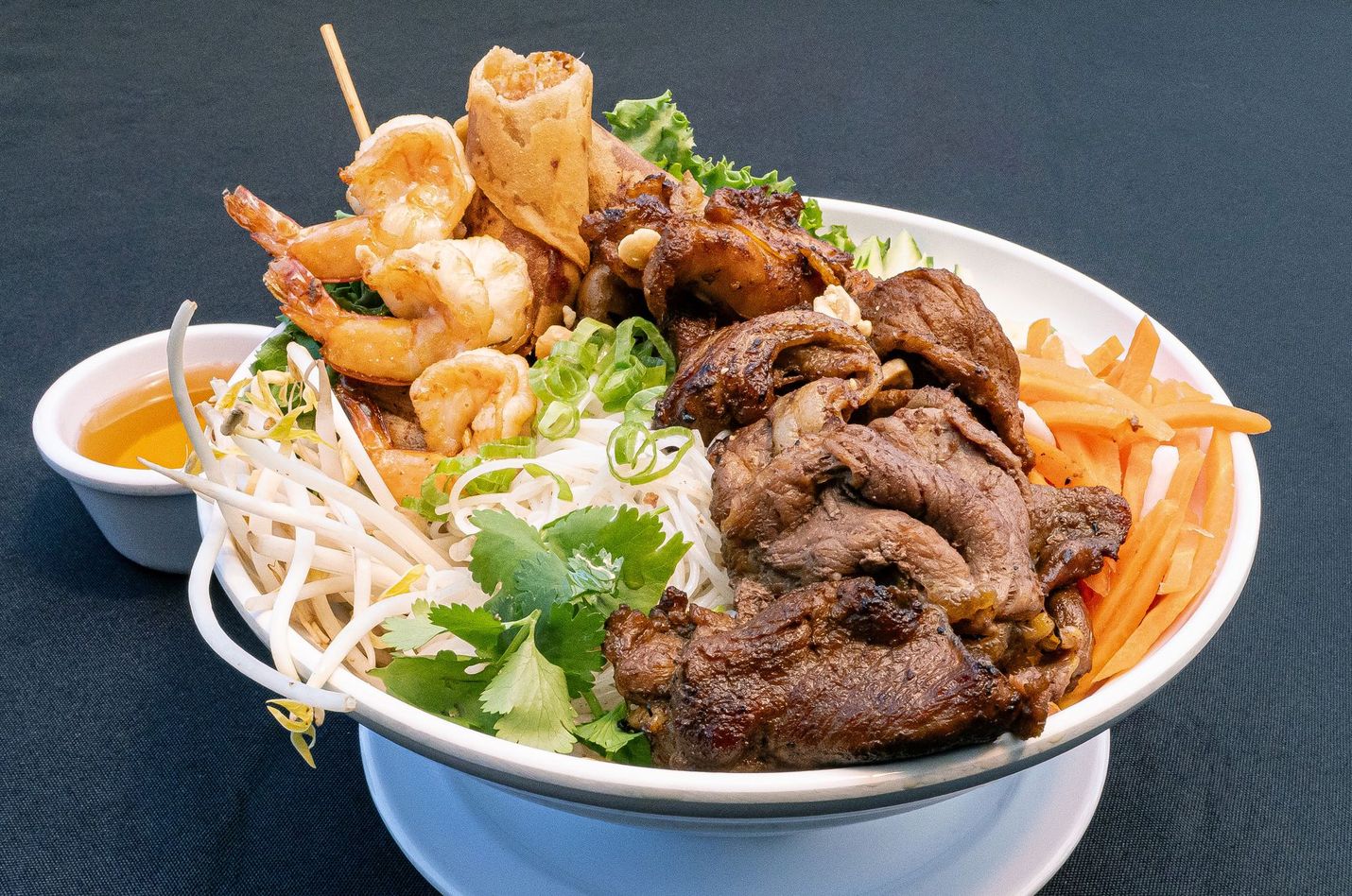 Bowl of Vietnamese noodle soup with grilled beef, shrimp, bean sprouts, herbs, and carrots
