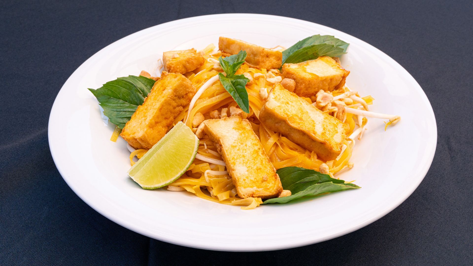 Fried tofu slices garnished with basil and lime on a white plate