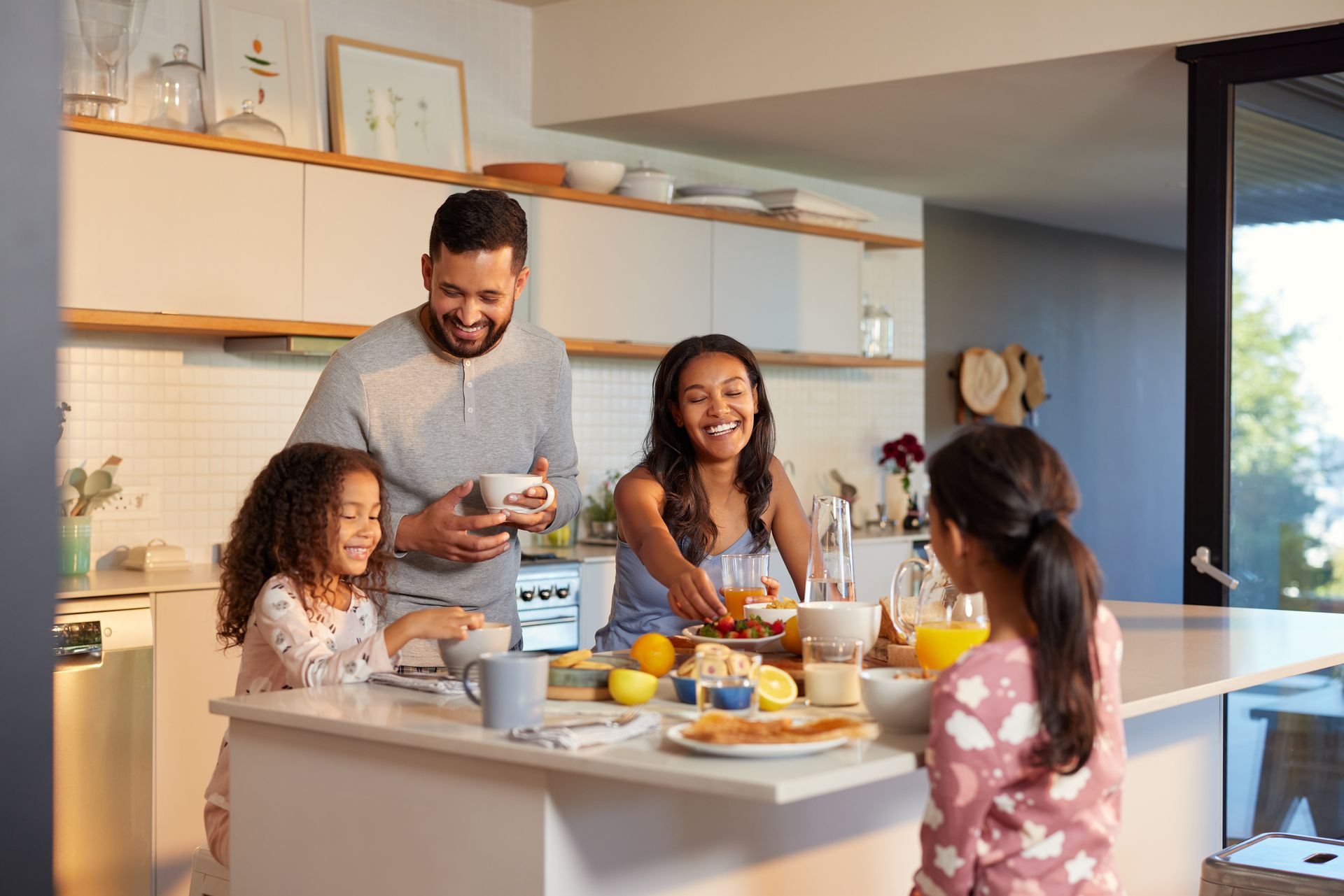 Family of four smiling while having breakfast at a kitchen island in a modern home.