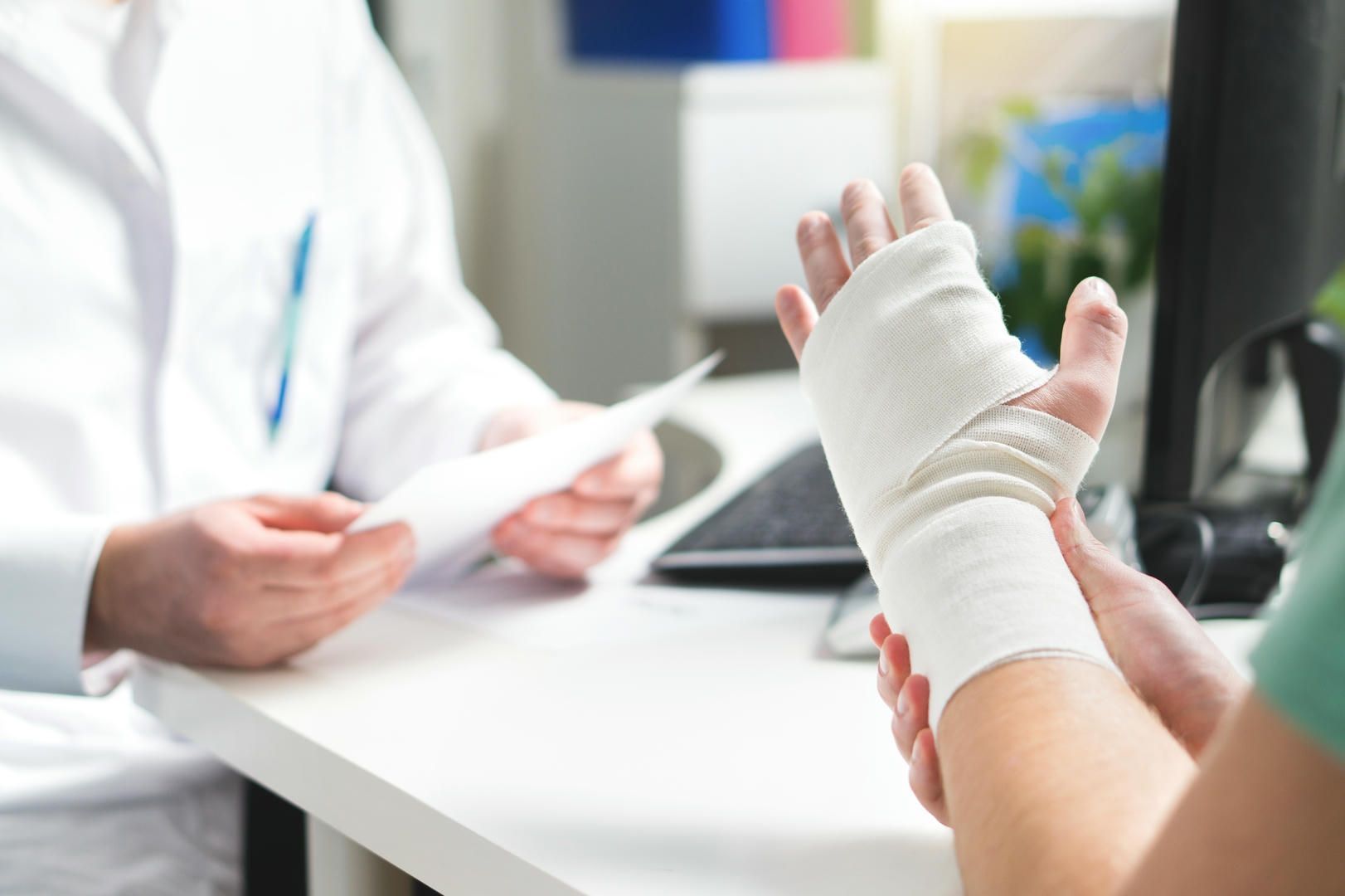 Person with bandaged hand at doctor's office; doctor holds a document.