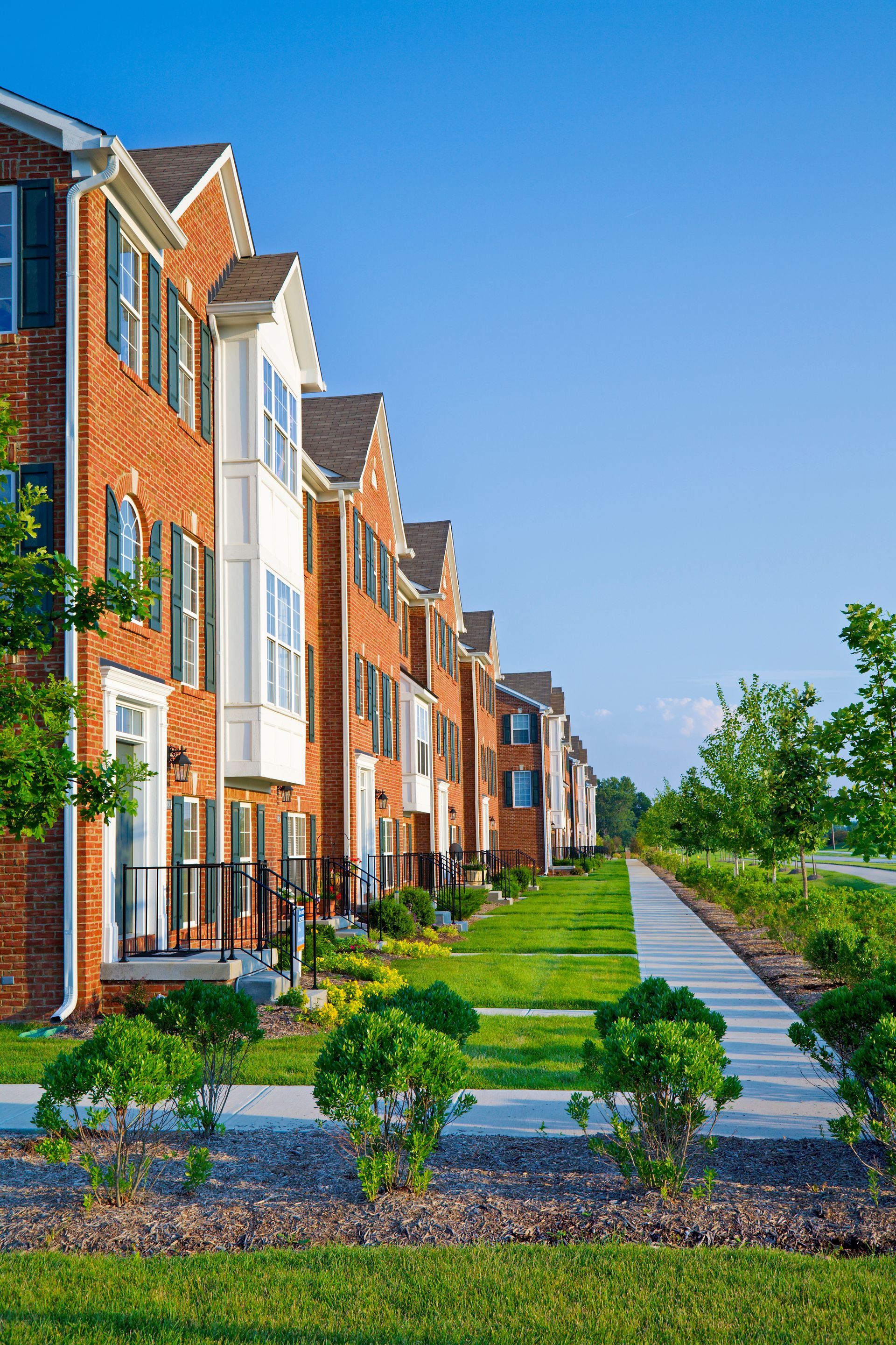 A row of brick apartment buildings with a sidewalk in front of them.