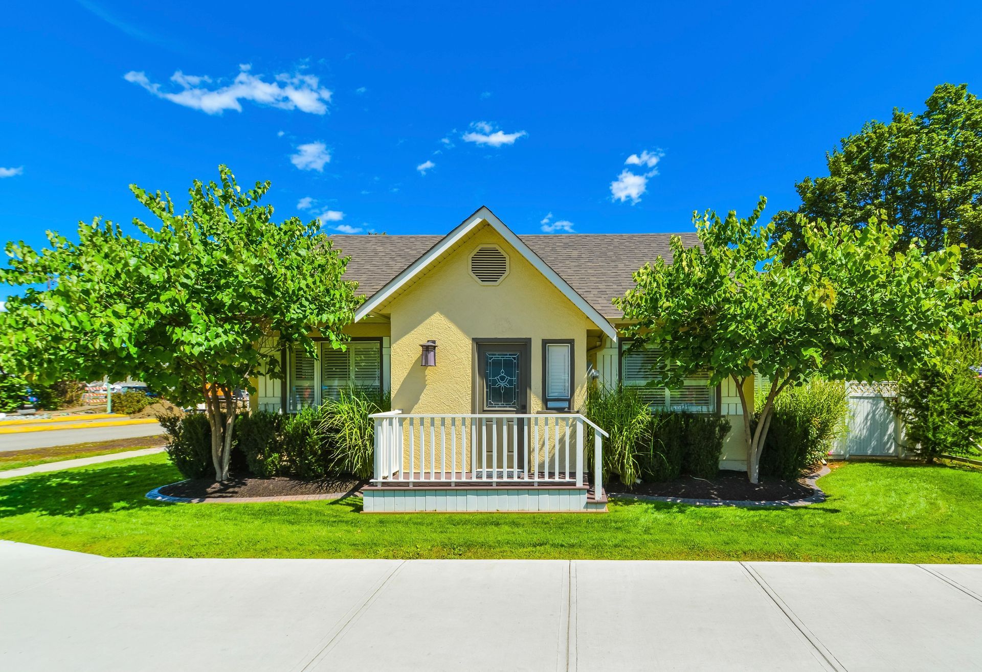 A small yellow house with a porch and trees in front of it.