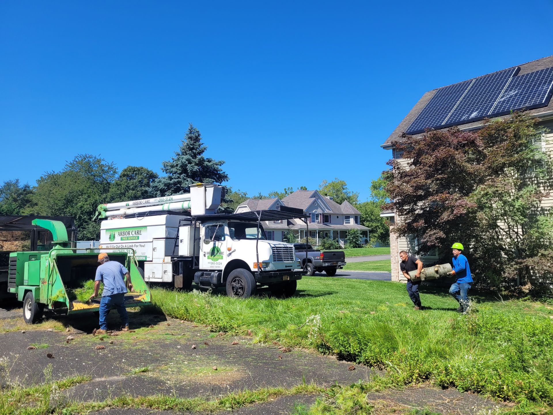 Utility crew working with trucks on a grassy street beside houses and solar panels
