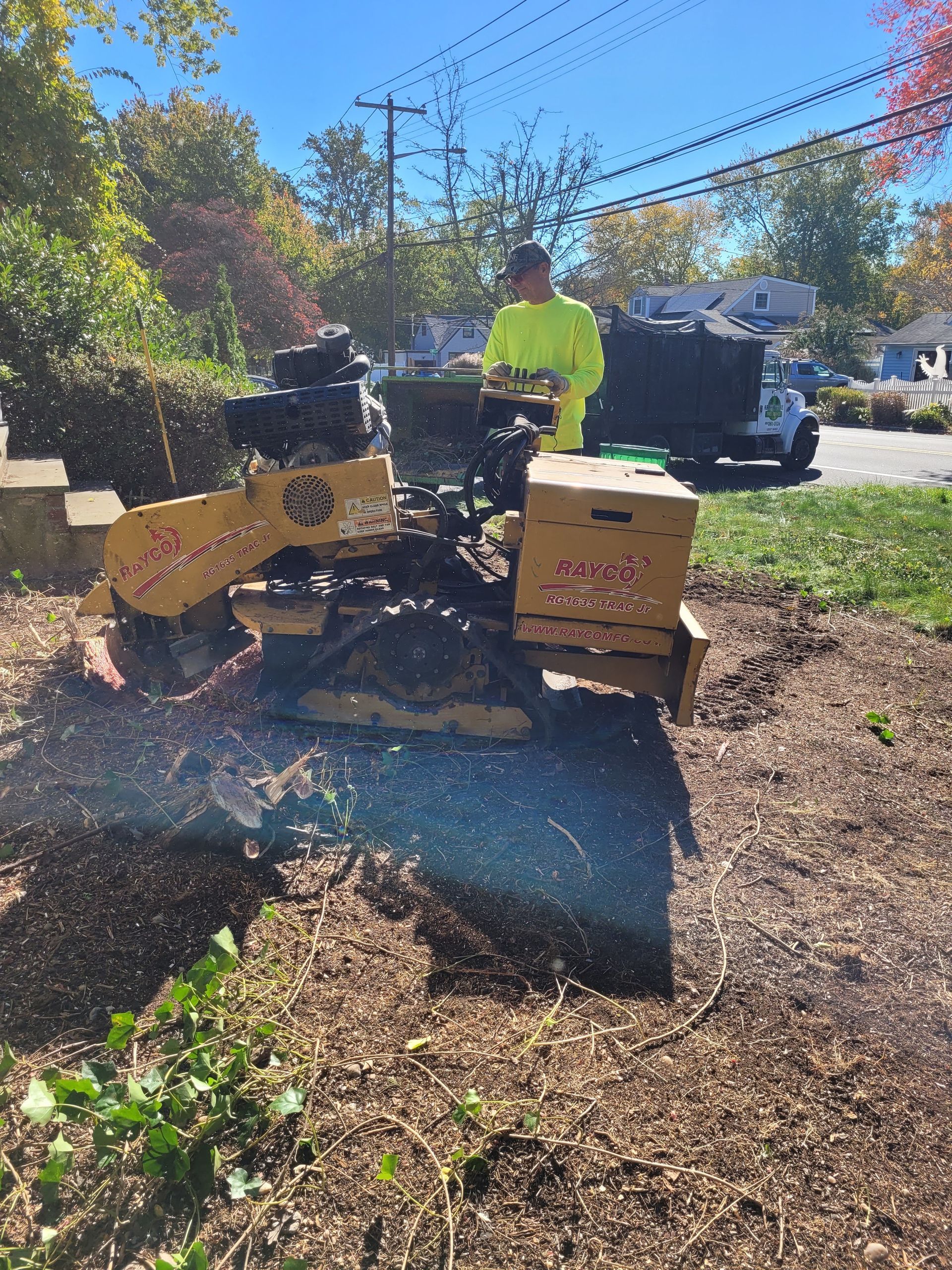 Person operating a yellow wood chipper outdoors beside cardboard boxes and a truck in sunny daylight