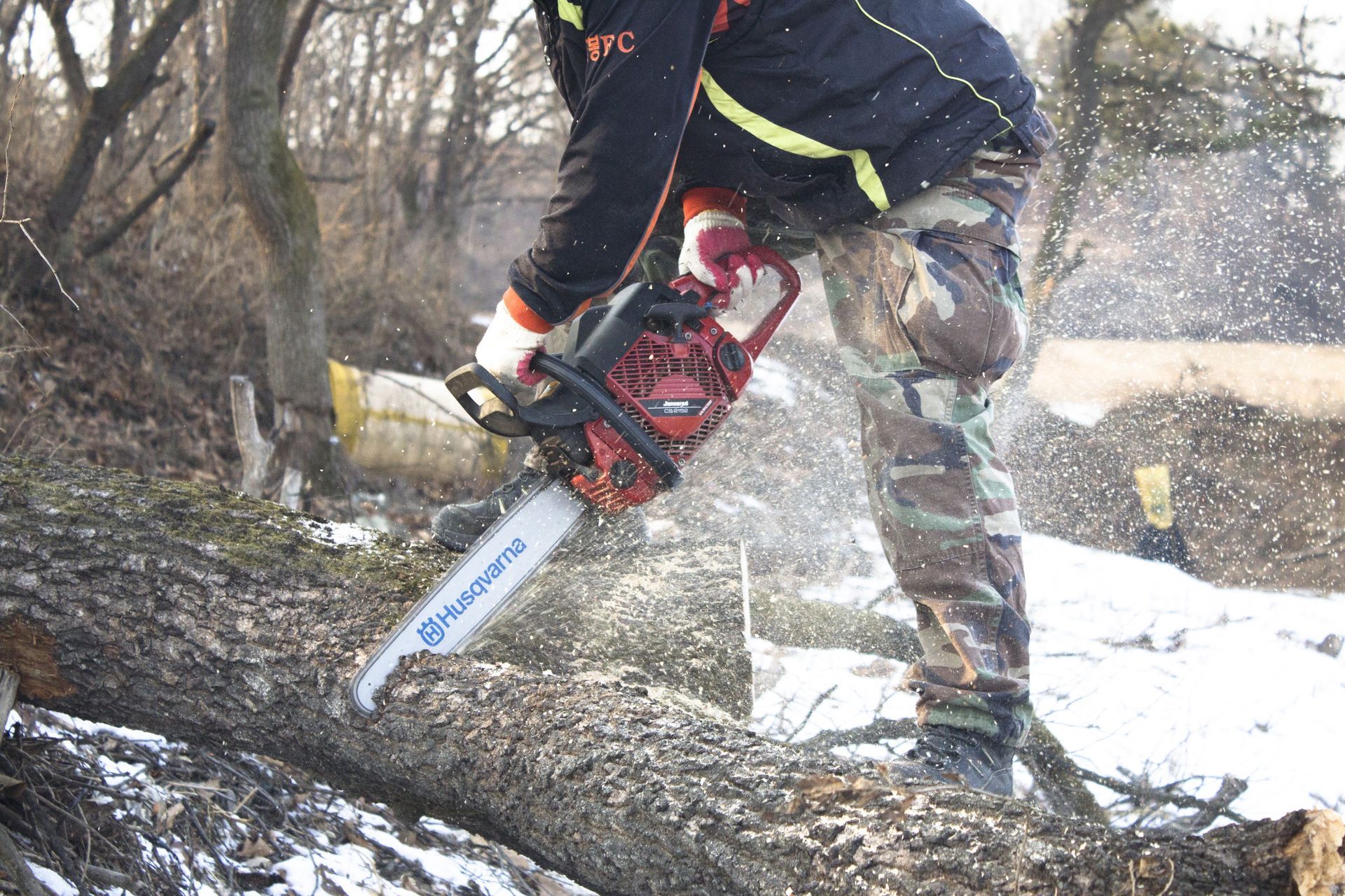 Person using a chainsaw to cut a fallen tree outdoors, with wood chips flying